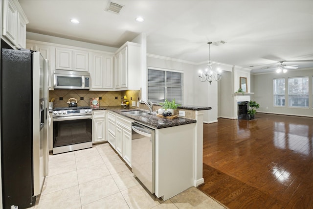 kitchen with sink, appliances with stainless steel finishes, kitchen peninsula, pendant lighting, and white cabinets