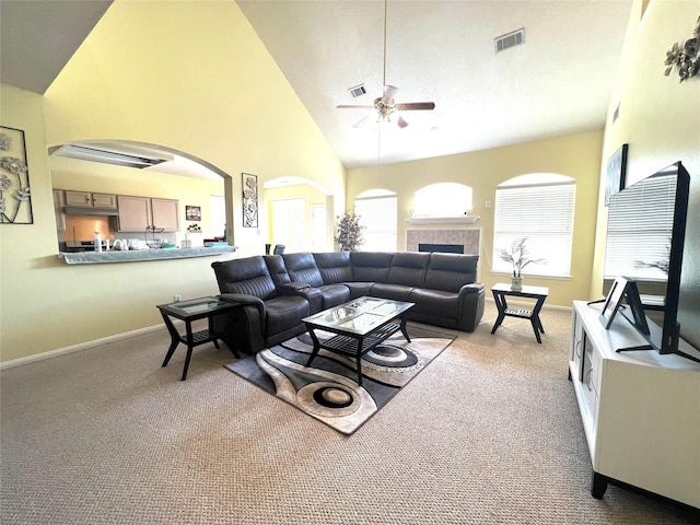 carpeted living room with ceiling fan, a fireplace, and high vaulted ceiling