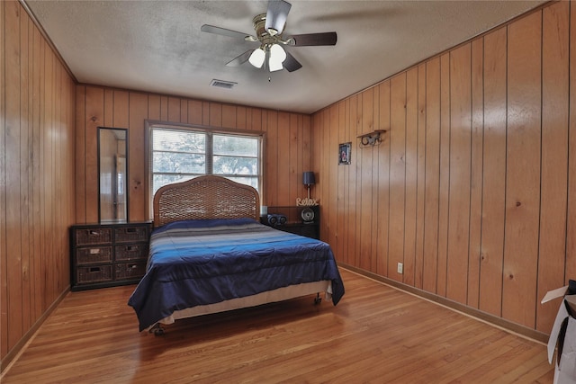 bedroom featuring ceiling fan, wooden walls, light hardwood / wood-style floors, and a textured ceiling