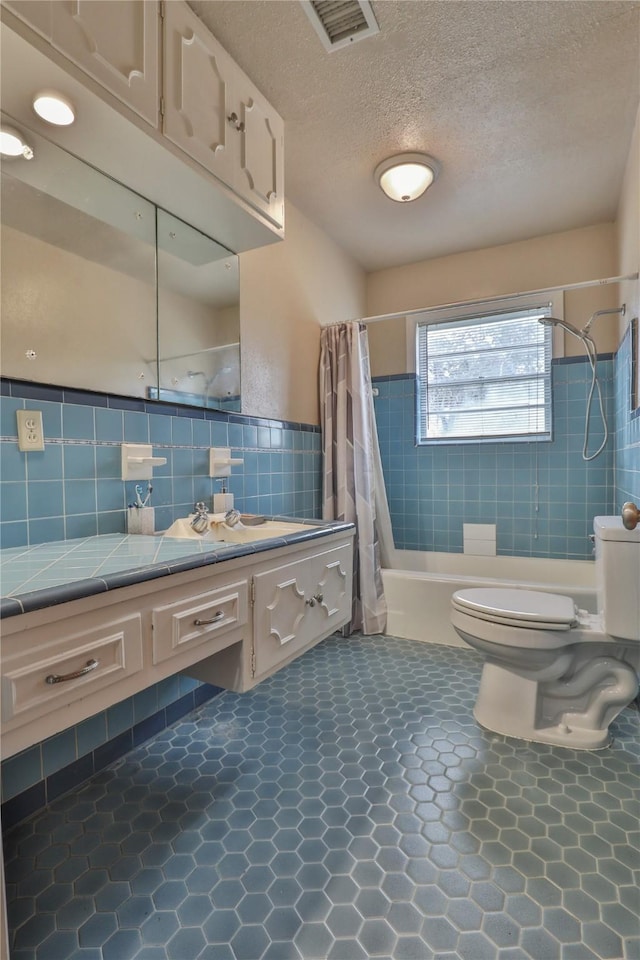 full bathroom featuring shower / tub combo with curtain, tile walls, vanity, a textured ceiling, and toilet