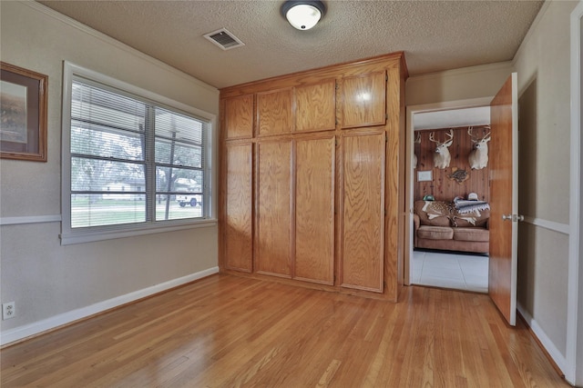 unfurnished bedroom with ornamental molding, a textured ceiling, and light wood-type flooring