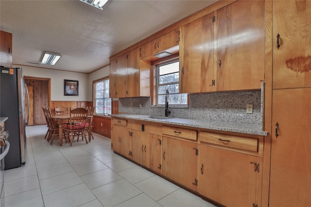 kitchen with stainless steel refrigerator, sink, backsplash, light stone counters, and a textured ceiling