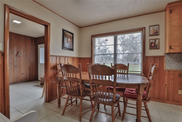 dining area with light tile patterned floors, wooden walls, ornamental molding, and a textured ceiling