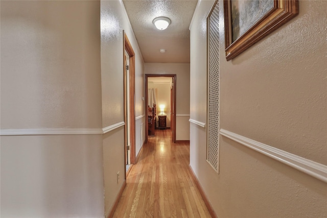 hallway with light hardwood / wood-style floors and a textured ceiling