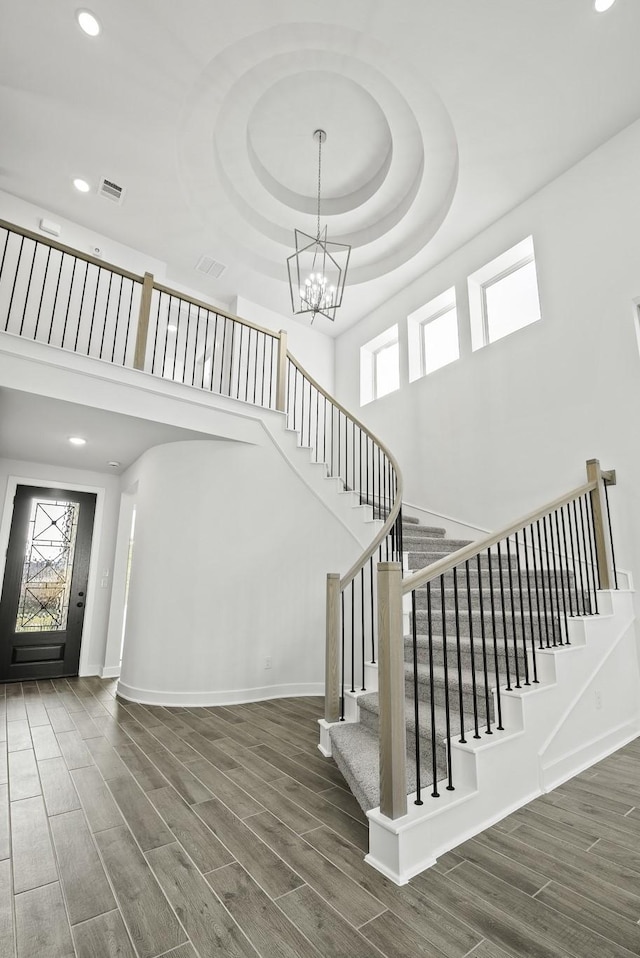 stairs with an inviting chandelier, hardwood / wood-style floors, and a towering ceiling