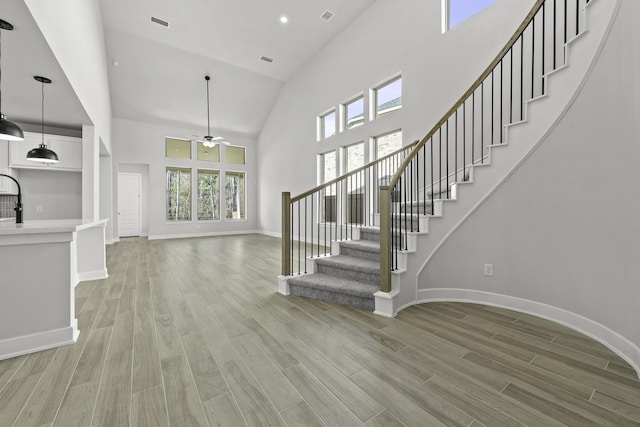 unfurnished living room with ceiling fan, high vaulted ceiling, and light hardwood / wood-style flooring