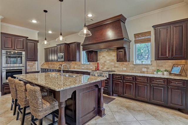 kitchen featuring an island with sink, stainless steel appliances, premium range hood, pendant lighting, and a sink