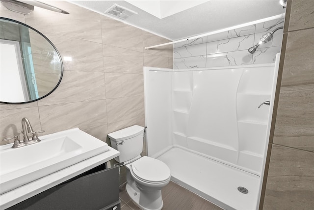 bathroom featuring tile walls, vanity, toilet, and walk in shower