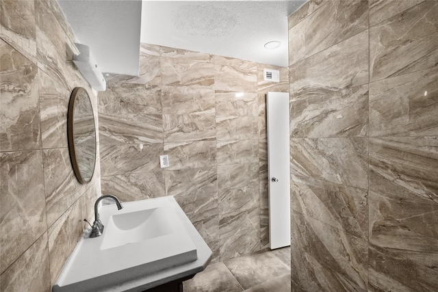 bathroom with tile walls, vanity, and a textured ceiling