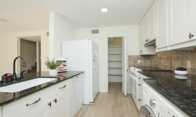 kitchen with sink, white appliances, white cabinetry, dark stone counters, and light wood-type flooring