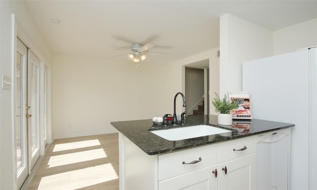 kitchen featuring sink, white appliances, white cabinetry, dark stone countertops, and light hardwood / wood-style floors