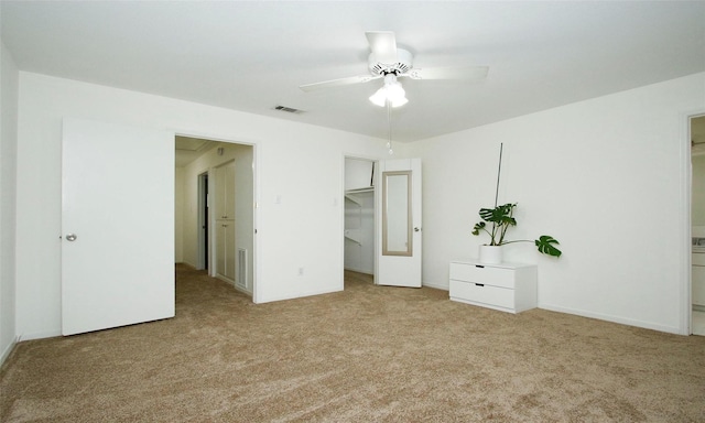 unfurnished bedroom with ensuite bath, a walk in closet, light colored carpet, a closet, and ceiling fan