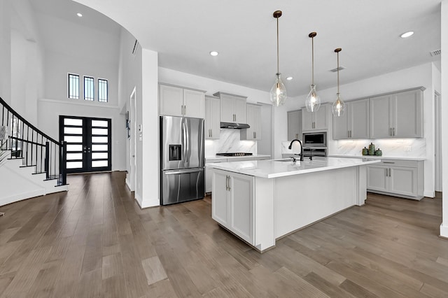 kitchen featuring sink, appliances with stainless steel finishes, hanging light fixtures, an island with sink, and french doors