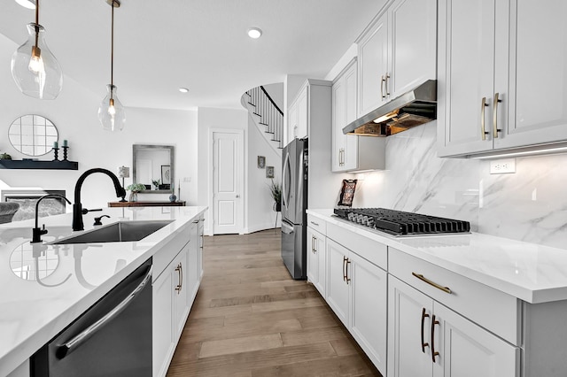 kitchen featuring sink, stainless steel appliances, light stone countertops, white cabinets, and decorative light fixtures