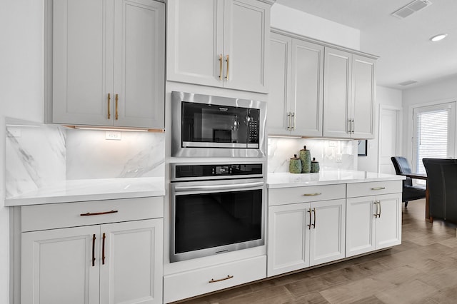 kitchen with tasteful backsplash, appliances with stainless steel finishes, light stone counters, and light hardwood / wood-style flooring