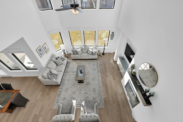 living room featuring ceiling fan, a towering ceiling, and light wood-type flooring