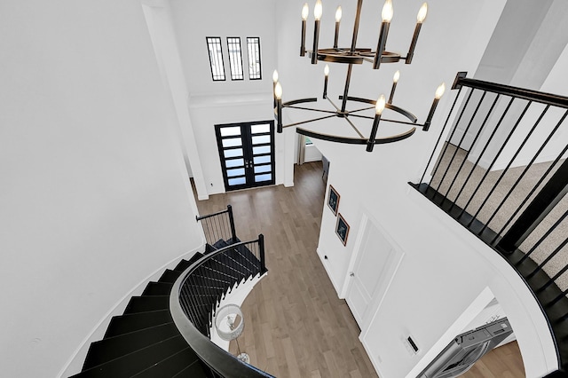 stairway with an inviting chandelier, wood-type flooring, and a high ceiling