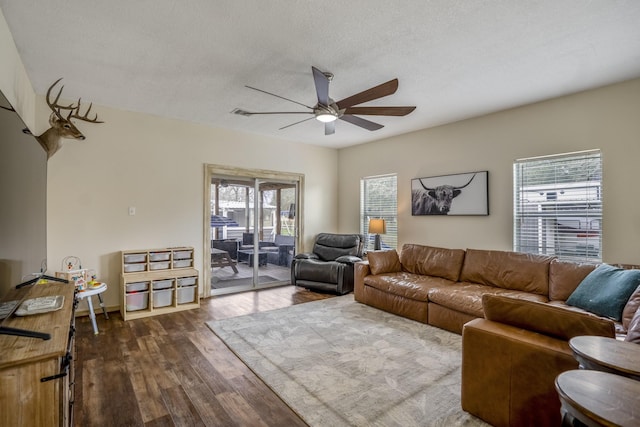 living room featuring dark wood-type flooring, ceiling fan, and a textured ceiling