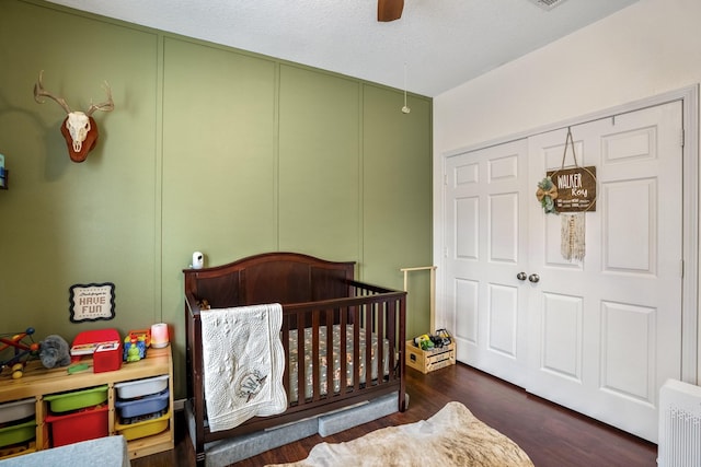 bedroom with a nursery area, dark wood-type flooring, and ceiling fan