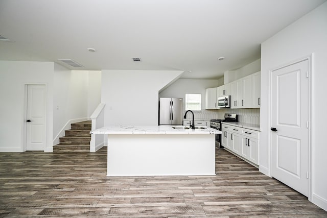 1415 E 35th St, Houston, TX 77022 - kitchen with stainless steel appliances, an island with sink, wood finished floors, white cabinetry, and light stone counters