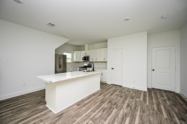 1415 E 35th St, Houston, TX 77022 - kitchen featuring appliances with stainless steel finishes, a center island with sink, dark wood-style flooring, white cabinets, and light stone countertops