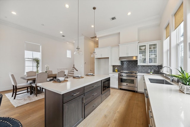 kitchen with glass insert cabinets, high end range, hanging light fixtures, light countertops, and a sink