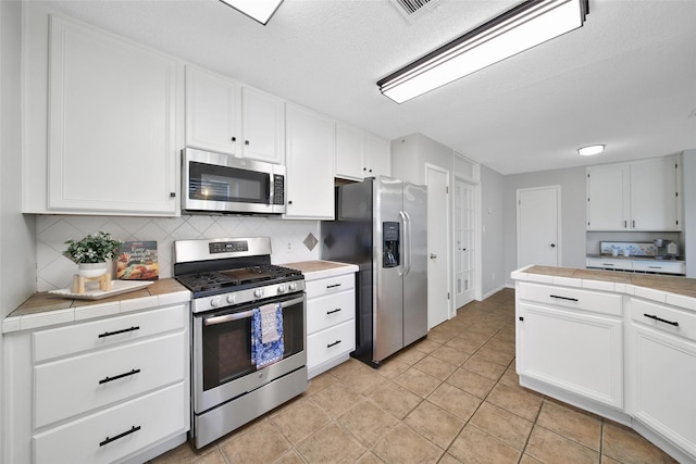 kitchen with appliances with stainless steel finishes, backsplash, a textured ceiling, white cabinets, and tile countertops