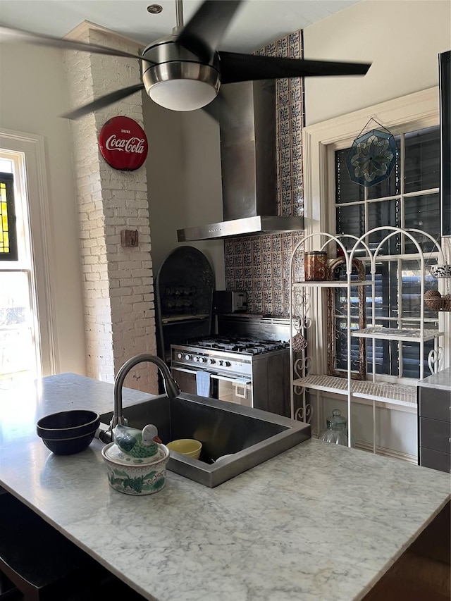 kitchen featuring stainless steel range with gas cooktop, sink, and wall chimney exhaust hood