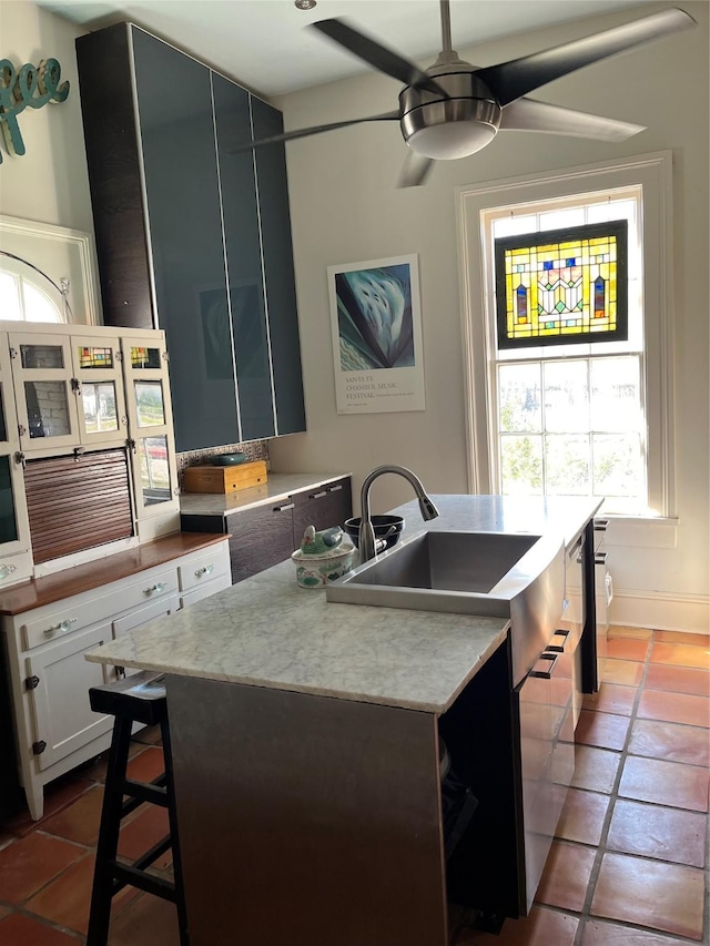 kitchen featuring tile patterned flooring, ceiling fan, an island with sink, and white cabinets