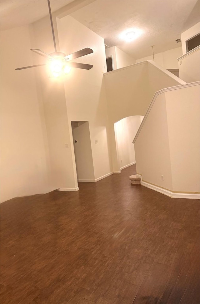 unfurnished living room with ceiling fan, dark hardwood / wood-style flooring, and a high ceiling