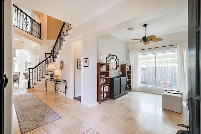 foyer entrance with a towering ceiling, ornamental molding, and ceiling fan