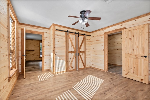 unfurnished bedroom with hardwood / wood-style flooring, ceiling fan, a barn door, and wooden walls