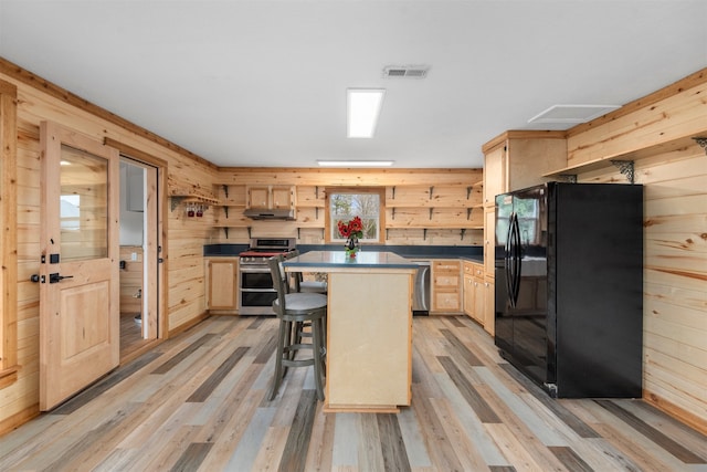 kitchen with black fridge, double oven range, light brown cabinetry, and a kitchen island