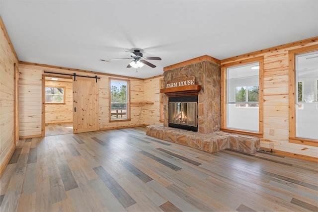 unfurnished living room featuring wood-type flooring, a barn door, a healthy amount of sunlight, and a stone fireplace