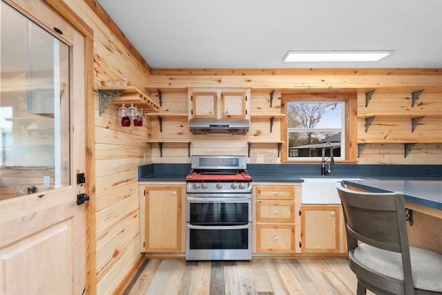 kitchen with wooden walls, light brown cabinetry, light hardwood / wood-style floors, and range with two ovens