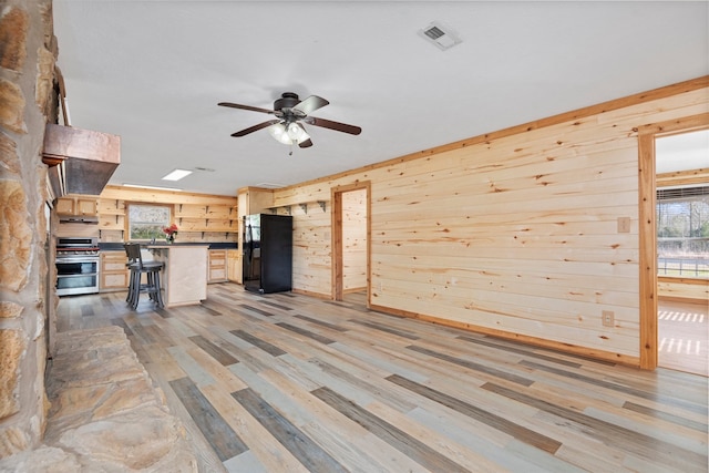 unfurnished living room with wooden walls, ceiling fan, and light wood-type flooring