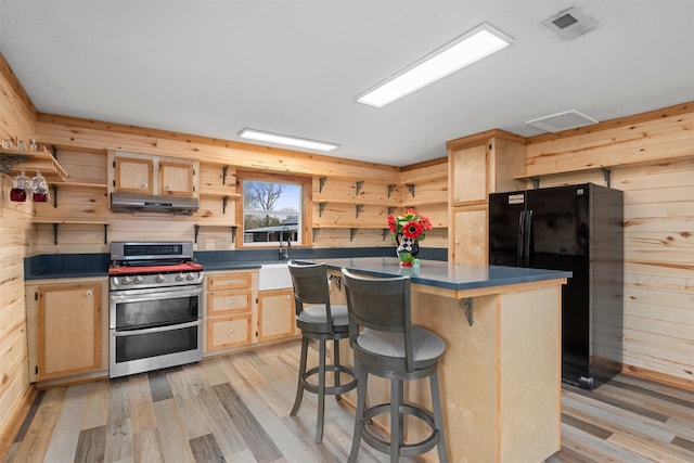 kitchen with a kitchen island, wooden walls, light brown cabinetry, range with two ovens, and black fridge