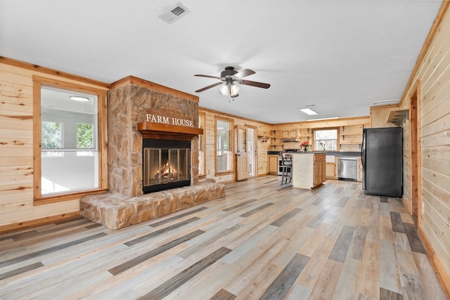 unfurnished living room with ceiling fan, a stone fireplace, light hardwood / wood-style floors, and wood walls