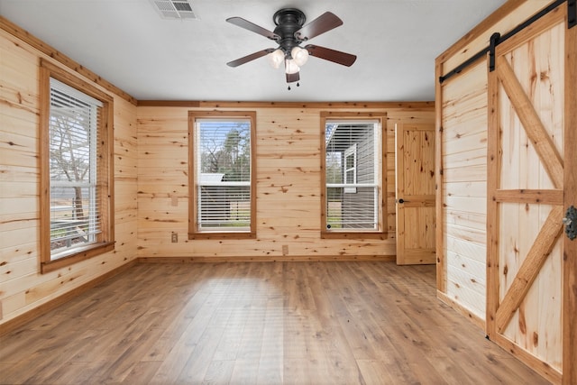 unfurnished room with hardwood / wood-style flooring, ceiling fan, a barn door, and wooden walls