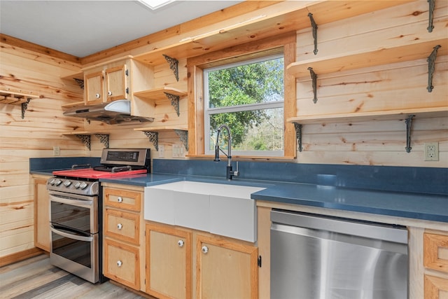 kitchen featuring light wood-type flooring, stainless steel appliances, sink, and wood walls