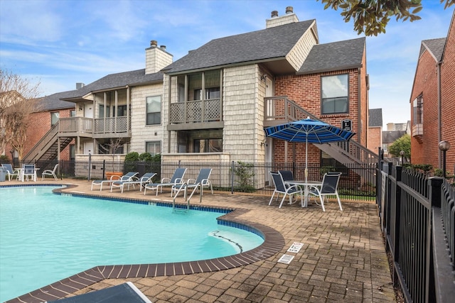 community pool with stairs, fence, and a patio