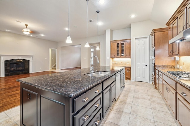 kitchen with sink, appliances with stainless steel finishes, hanging light fixtures, a fireplace, and a center island with sink