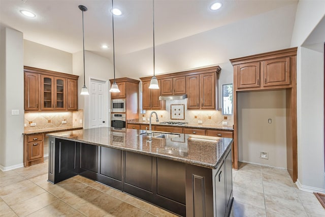 kitchen with sink, hanging light fixtures, a center island with sink, dark stone counters, and stainless steel appliances