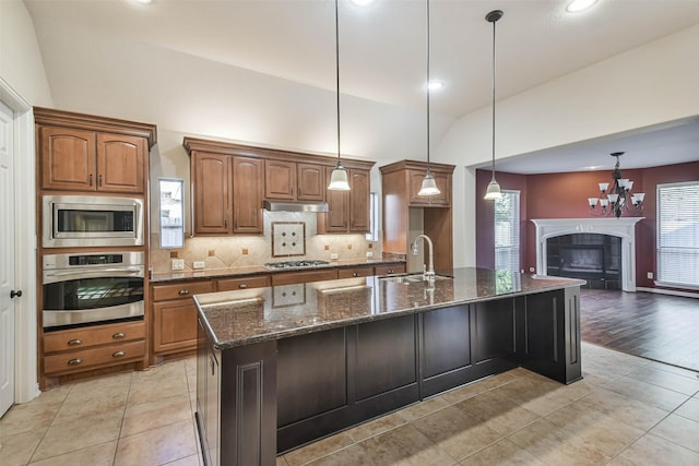 kitchen featuring appliances with stainless steel finishes, decorative light fixtures, sink, dark stone counters, and a large island with sink