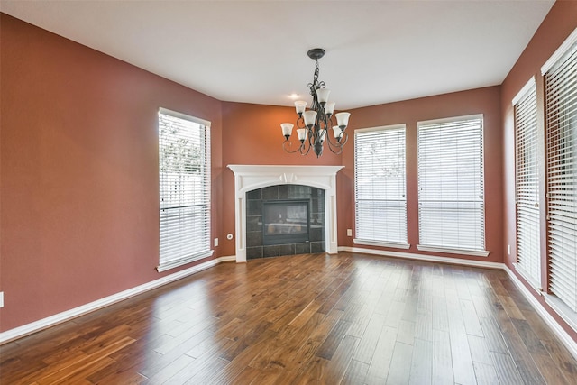 unfurnished living room with an inviting chandelier, dark hardwood / wood-style flooring, and a tiled fireplace