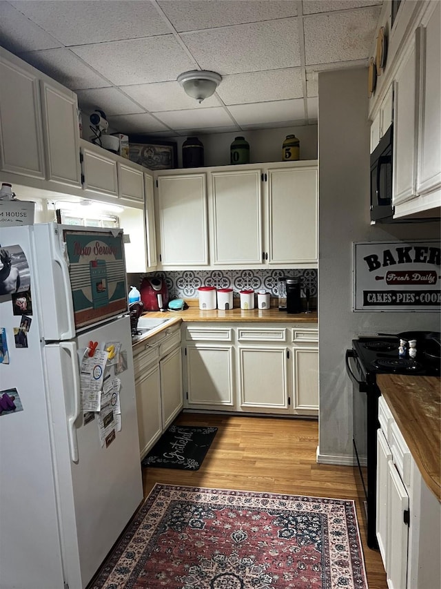 kitchen featuring a paneled ceiling, butcher block counters, white cabinets, black appliances, and light wood-type flooring