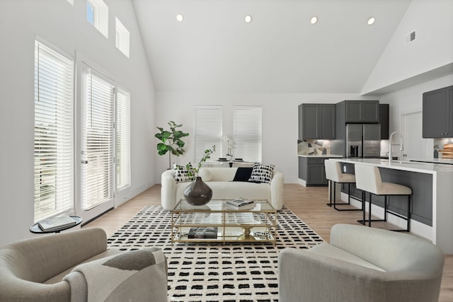 living room with sink, high vaulted ceiling, and light wood-type flooring