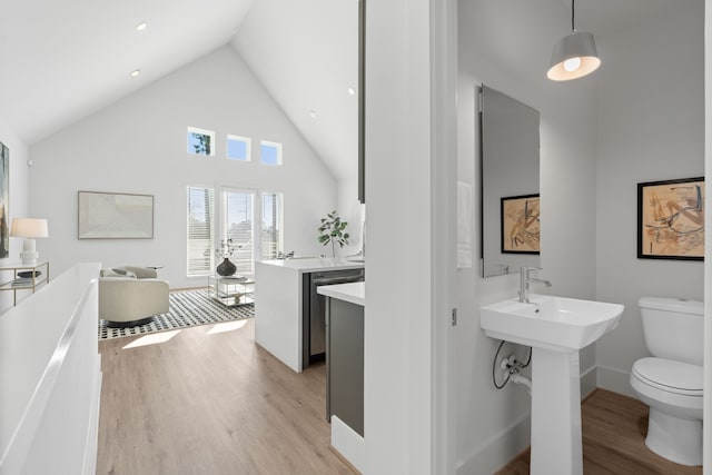 bathroom featuring high vaulted ceiling, toilet, a sink, wood finished floors, and baseboards