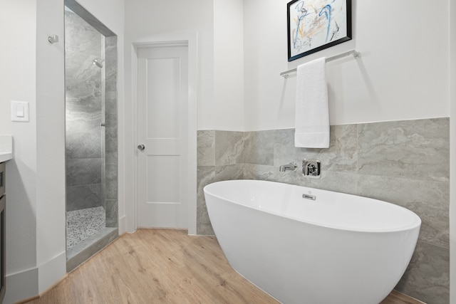 full bath featuring wood finished floors, a freestanding bath, vanity, a shower stall, and tile walls