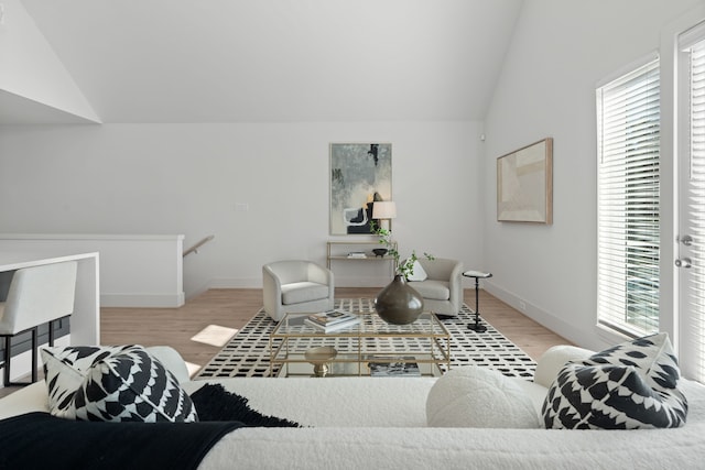 living area featuring vaulted ceiling, light wood-type flooring, and baseboards